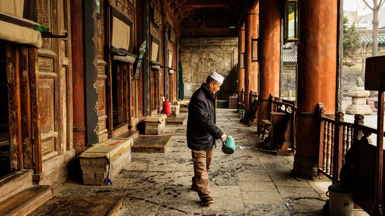 西安清真大寺，一个人给大殿外的地板洒水。Elsewhere in the city, a man waters the floor outside the main prayer hall of the Great Mosque of Xian..jpg